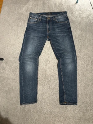 Lean Dean Nudie - Snygga blå jeans från Nudie Jeans med klassisk femficksdesign och orangea sömmar. Jeansen har en rak passform och är tillverkade i slitstarkt denimtyg av bomull. Perfekta för en avslappnad och trendig look.