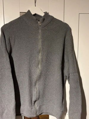 Grå ribbstickad ziptröja - Säljer en grå ribbstickad tröja med dragkedja framtill och hög krage