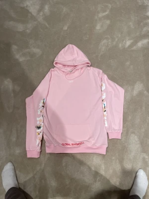 Off White hoodie  - Snygg rosa hoodie från Off-White med blom- och insektstryck på ärmar och rygg. Texten 'GLOBAL WARMING?' syns framtill och baktill. Klassisk huva och magficka. Perfekt för dig som gillar streetwear och unika detaljer. 