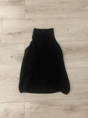 Svart ärmlös halterneck topp - Snygg svart halterneck topp med hög krage och ärmlös design och öppen rygg Toppen har en stilren och minimalistisk look, perfekt att matcha med jeans eller kjol. Tillverkad i ett mjukt och följsamt material som känns bekvämt mot huden.