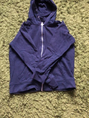 Mörkblå hoodie med dragkedja - En enkel och stilren mörkblå hoodie med dragkedja framtill och två fickor. Hoodien har huva och ribbade muddar vid ärmar och nederkant. Perfekt för en avslappnad look. Materialet känns mjukt och bekvämt, troligen bomull eller bomullsblandning.