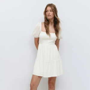 Studentklänning  - Superfin vit kortklänning med puffärmar och öppen rygg som knyts med en stor rosett. Klänningen har en lätt volang nertill och är perfekt för sommarens alla tillfällen. Tillverkad i ett mjukt och luftigt material. Aldrig använd helt ny,