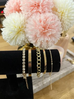 Guld Armband Set - Säljer ett set med fem snygga armband i guldfärg. Setet innehåller ett armband med gnistrande stenar, ett slätt metallarmband, ett kedjearmband, ett smalt armband med räfflad yta och ett tunt kedjearmband. Perfekt för att mixa och matcha till olika looks. Helt ny aldrig använd. Rostfritt stål. Justerbar.