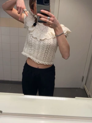 Vit spetsig croppad blus med volang - Supersöt vit croppad blus med stora volangdetaljer och spetsmönster. Blusen har korta ärmar och en bred, dekorativ krage som ger en romantisk vibe. 