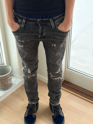 Svarta slitna skinny jeans från Jack and Jones  - Säljer ett par svarta skinny jeans med slitningar och distressed detaljer. Jeansen har låg midja och klassisk femficksmodell. Snygg tvätt med ljusa partier och råa kanter för en edgy look.