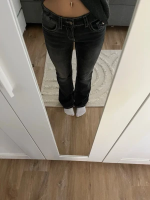 Svarta bootcut jeans med kontrastsömmar - Säljer ett par svarta bootcut jeans från Gina tricot med vita kontrastsömmar och klassisk femficksdesign. Jeansen har låg midja och är tillverkade i ett stretchigt denimtyg som sitter snyggt på kroppen. Perfekta för en avslappnad men trendig look. Byxorna är i storlek 152.