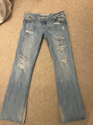 Ljusblå lågmidjade bootcut jeans från Hollister - Snygga ljusblå lågmidjade bootcut jeans med slitningar från hollister som är köpta second hand. Passar mig som brukar ha S (står storlek 7R) Lite långa på mig som är 165 därav slitningar nedtill. 