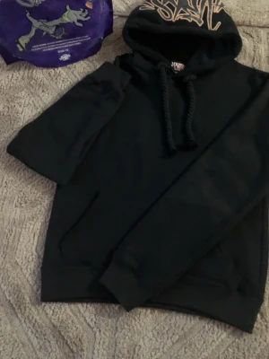 Syns world hoodie - Säljer en svart hoodie från syna world med stort tryck i beige på huvan. Hoodien har en klassisk känguruficka framtill, breda snören och ribbade muddar vid ärmslut och nederkant. Perfekt för en avslappnad och cool stil.