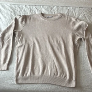 Beige stickad tröja från Zara - Snygg beige stickad tröja från Zara med rund halsringning och ribbade muddar vid ärmslut och nederkant. Tröjan har en enkel och stilren design som passar till det mesta. Perfekt för lager på lager och enkel att matcha.