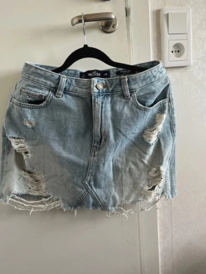 Ljusblå jeanskjol från Hollister - Ljusblå jeanskjol från Hollister med slitna detaljer. Storlek 28.