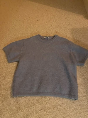 Ljuslila stickad t-shirt - Kortärmad stickad tröja i ljusblå med rund halsringning. Tröjan har en boxig passform och är gjord i ett mjukt, fluffigt material som känns skönt mot huden. Perfekt för lager-på-lager eller som statement-piece.