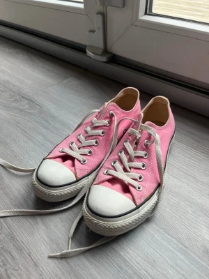 Rosa Converse All Star sneakers - Säljer ett par klassiska Converse All Star sneakers i rosa canvas med vita snören och tåhätta. Skorna har låg profil och den ikoniska All Star-loggan baktill. Perfekta för dig som vill ha en färgklick till din outfit.
