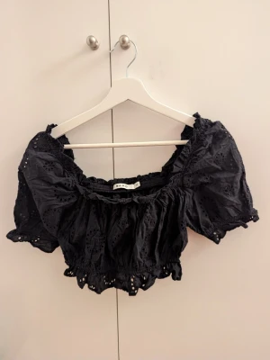 Svart broderad blus från NA-KD - Säljer en svart blus från NA-KD i storlek 34. Toppen har korta puffärmar, broderade detaljer och volangkant. Kort i modellen. Materialet är lätt och luftig bomull, perfekt för varmare dagar. Söt och trendig modell med elastiska partier för skön passform.                                                                       Pris kan diskuteras vid smidigt köp 😊.                        Köparen står för frakt! 