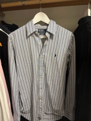 Randig skjorta från Polo Ralph Lauren - Klassisk skjorta från Polo Ralph Lauren.Skjortan har lång ärm, knappar framtill och broderad logga på bröstet. Custom fit-modell som ger en snygg passform. Perfekt för en stilren look.