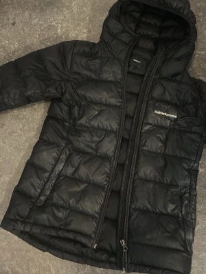 Svart Peak Performance jacka  - Snygg svart dunjacka från Peak Performance med huva och quiltad design. Jackan har dragkedja framtill och två sidofickor. Perfekt för kalla dagar och enkel att matcha med olika outfits.
