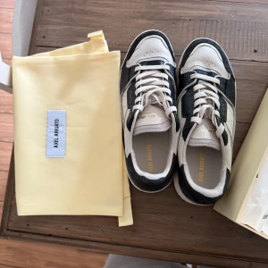 Axel Arigato sneakers mörkblå/vit - Snygga sneakers från Axel Arigato i mörkblå och vitt skinn med detaljer i mocka. Klassisk låg modell med rund tå, vita snören och diskret guldtext på sidan. Kommer med originalkartong och dustbag. Perfekta för en stilren och modern look. Endast använt en gång 