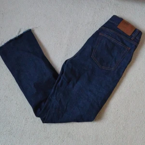 Mörkblå raw denim från Human Scales - Snygga mörkblå jeans från Human Scales i rak modell med råa, fransiga benslut. Klassisk femficksdesign, orange kontrastsömmar och läderpatch bak i midjan. Perfekta för dig som gillar stilrena jeans med en edge. Skicket är bra men avklippta. Längd 106cm. Priset är verkligen inte hugget i sten ✌️❤️