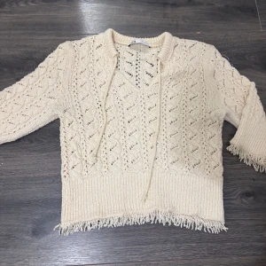 Beige stickad tröja med snörning Zara  - Beige stickad tröja från zara  med snyggt hålmönster, v-ringning och snörning vid halsen. Tröjan har trekvartsärm och fransad nederkant för en chill och trendig look. Perfekt till jeans eller kjol för en avslappnad stil. Aldrig använd pris kan diskuteras prislappen har gått av .💓!!
