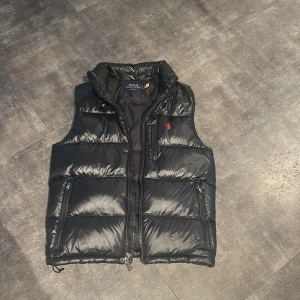 Polo Ralph Lauren Water-Repellent Down Vest - Hej! Säljer nu denna snygga Polo Ralph Lauren väst i nytt skick, bara använt 1 gång. Den har inga defekter och kostar 3500 nypris. En perfekt väst nu för hösten och passar perfekt med en hoddie under eller en snygg tröja, kan även användas som lager under vintern. Snälla fråga vid minsta lilla fundering. Jag som har på den är 175 cm och passar perfekt, passar perfekt hela vägen up till 185 cm!