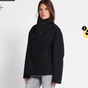Svart ullkappa med hög krage - Säljer en svart grå kappa lite med oversized passform och hög krage. Jackan har stora knappar framtill och raka, långa ärmar. Perfekt för dig som gillar minimalistisk och stilren look. Snygg att bära öppen eller knäppt hela vägen upp. Helt oanvänd