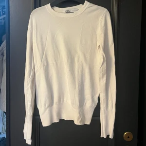 Vit långärmad tröja från Zara - Vit långärmad tröja från Zara i mjukt material. Tröjan har rund halsringning och snygga knappar som detalj vid ärmsluten. Perfekt för dig som gillar stilrena och enkla plagg med en twist.