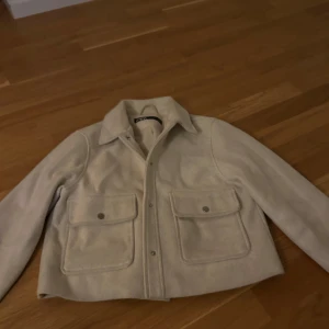 Beige kappa från Zara  - Snygg beige kappa från Zara i  med två stora fickor framtill och tryckknappar. Jackan har klassisk krage och är helfodrad för extra komfort. Perfekt att slänga på sig över en hoodie eller t-shirt för en chill look. Mycket bra skick. Priset går absolut att diskutera vid rimliga priser 