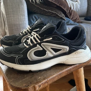  B30 svarta och vita sneakers - Snygga  B30 sneakers i svart och vitt med tydliga CD-loggor på sidan, häl och sula. Skorna har mesh och skinnpaneler, vita snören och en chunky vit sula. Perfekta för dig som gillar exklusiva och trendiga sneakers med sportig vibe.