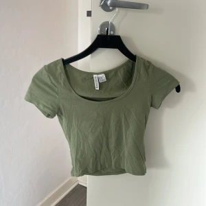 Olivgrön croppad topp  - Snygg olivgrön croppad topp från HM med rundad urringning och korta ärmar. Perfekt för dig som gillar en enkel men trendig stil. Tunn och mjuk bomull som känns skön mot huden.