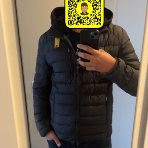 Svart dunjacka från Parajumpers S - Svart dunjacka från Parajumpers i storlek S. Jackan är superlätt och har en klassisk quiltad design med dragkedja framtill, hög krage och en gul detalj vid halsen. Perfekt för kyliga dagar och enkel att matcha med allt. Den har dock ett litet hål på ärmen men de syns knappt och ett pyttelitet hål på ryggen och den syns inte alls annars är den riktigt bra skön och varm till hösten eller vintern 