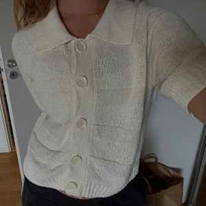 Vit stickad kofta med kort ärm - Säljer en vit stickad kofta med korta ärmar och stora, snygga knappar framtill. Koftan har en bred krage och ribbade muddar nedtill. Perfekt för dig som gillar en chill och stilren look till våren eller sommaren. Köpt på lindex för 499kr 🤍