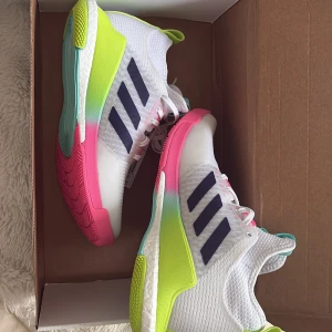 Adidas sneakers i vitt med neon och rosa - Färgstarka Adidas sneakers med vit mesh, svarta ränder och detaljer i neon-gult, rosa och turkos. Snygg sportig vibe med snörning och platt sula. Perfekta för dig som vill sticka ut på gymmet eller i stan.