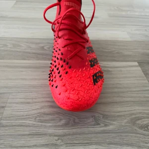 Adidas Predator röda fotbollsskor - Säljer ett par Adidas Predator elite som tillhört Linda sembrant landslags spelar. fotbollsskor i rött med svarta detaljer och taggar på ovandelen för extra grepp. Skorna har snörning, hög krage och mönstrad sula för bästa fäste på planen. Materialet är syntet och textil, perfekt för dig som vill sticka ut på matchen.