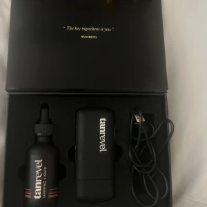 Tanrevel Face Mist Kit - Tanrevel Face Mist Kit med en svart sprayenhet, USB-sladd och en flaska tanning liquid. Perfekt för att få en naturlig solkysst glow på nolltid. Snygg förpackning i svart med roséguld-detaljer. Enkel att använda och smidig att ta med sig. Dock är den använd men fungerar fortfarande galant. Box,laddare och apparaten medkommer samt oljan då det finns lite grann kvar i den.