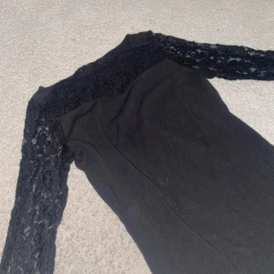 Svart kort klänning med spetsärmar - Snygg svart klänning med långärmade spetsdetaljer. Modellen är figurnära och har en enkel, stilren design med transparent spets upptill och på ärmarna. Perfekt för dig som gillar en elegant look med lite edge. Passar dig som vill sticka ut med coola detaljer.