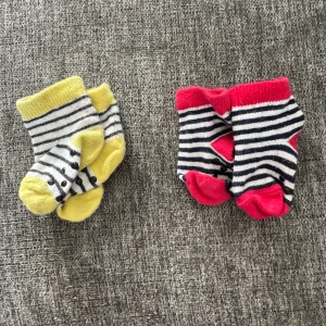 Randiga strumpor, 2-pack - Två par söta strumpor, ena paret med gul kant och tå, andra med rött. Båda har svartvita ränder och halkskydd under foten. Perfekt för små fötter som vill ha lite färg och mönster. Mjukt material som känns skönt mot huden.