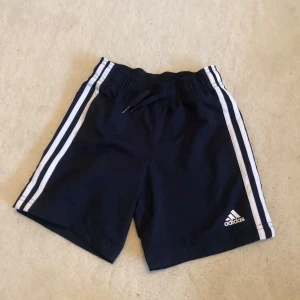 Adidas marinblå träningsshorts barn - Snygga marinblå träningsshorts från Adidas med klassiska vita ränder längs sidorna och logga framtill☺️🦋De har elastisk midja. strl: 6-7 år💕122 cm💗 använd några få gånger (de  är som nya) väldigt bra skick🥰