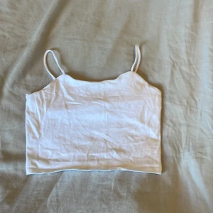 Vit croppad linnetopp - En enkel och fräsch vit croppad linnetopp med tunna axelband. Perfekt för varma dagar eller att styla lager på lager. Toppens raka modell gör den lätt att matcha med både jeans och kjol.