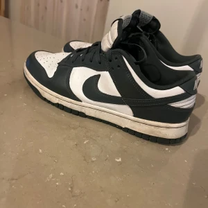 Nike Dunk Low mörkgrön/vit sneakers - Nike Dunk Low sneakers i svart och vitt med klassisk Nike loggan  på sidorna. Skorna har snörning, perforerad tåbox och platt sula. Ovandelen är i skinn och de har en låg siluett använda max 10 gånger perfekt nu till hösten kom gärna med bud mvh Edvin