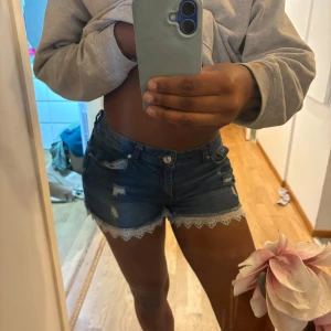 Blå jeansshorts med spetskant - Snygga blå jeansshorts med slitna detaljer och söt vit spetskant längst ner. Klassisk femficksmodell och låg midja.