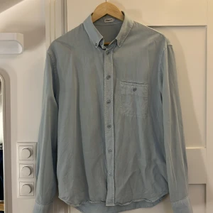 Ljusblå skjorta från Filippa K - Snygg ljusblå skjorta från Filippa K med klassisk krage och knappstängning hela vägen. Skjortan har en bröstficka med knapp och långa ärmar med manschett. Perfekt för en clean och stilren look. Storlek 46