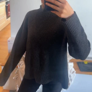 Mörkgrå stickad tröja med loose fit - Mysig mörkgrå stickad tröja med loose passform och ribbade muddar vid ärmslut och hals. Perfekt för kyliga dagar och enkel att matcha med jeans eller leggings. Klassisk modell med lång ärm och rund halsringning.