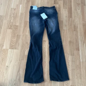 Bootcut jeans från Bershka, svart/grå - Bootcut jeans från Bershka i en snygg tvättad svart/grå färg. Klassisk femficksmodell med dragkedja och knapp framtill. Jeansen har en bootcut-passform som ger en schysst siluett och är tillverkade i mjukt jeansmaterial.