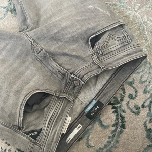 Replay grå jeans med slitningar - Grå jeans från Replay med snygga slitningar och lagade detaljer på benen. Klassisk femficksmodell med raka ben och diskret tvättad look. Märkt med Sustainable Lab. Perfekta för dig som gillar en avslappnad och trendig stil, pris kan diskuteras🎯