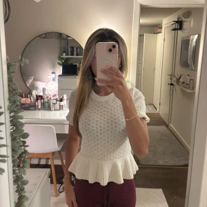 Vit stickad blus med volangkant - Supersöt vit stickad blus med korta ärmar och volangkant nedtill. Den har ett fint hålmönster och rund halsringning. Perfekt för dig som gillar en feminin och trendig look.