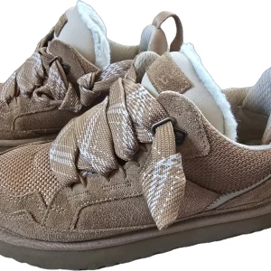 Ugg lowmel chestnut, strl 40 - Bekväma och stilrena sneakers från Ugg i en fin brun färg. Perfekt för en avslappnad men trendig look. Skorna har en unik design med dekorativa snören och en mjuk, vadderad insida för extra komfort. Extra oanvända bruna skosnören skickas med. Storlek 40 (jag har normal strl 39). Orginalkartong följer med.