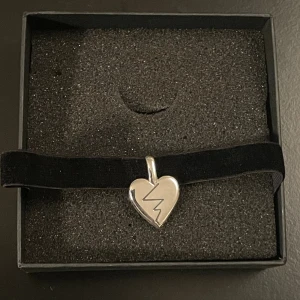 Halsband/choker Efva Attling, Miriam Bryant x Högdalen - Unikt halsband/choker med ett hjärthänge (broken heart) i silver på svart band. Kommer i en snygg ask med 'Sönder' och Miriam Bryant-logga. Perfekt statement piece för dig som gillar edgy och personliga accessoarer.