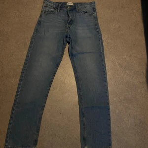 Blåa relaxed jeans Jack & Jones 29/32 - Säljer ett par blåa relaxed fit jeans från Jack & Jones, modell Chris. Klassisk femficksdesign, raka ben och normalhög midja. Jeansen är i bomull och har snyggt tvättad look med gul kontrastsöm. Perfekta för en chill och avslappnad stil.