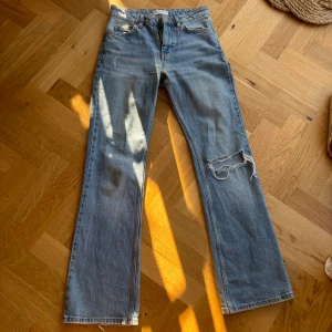 Ljusblå raka jeans med slitning - Säljer ett par ljusblå jeans med rak passform och snygg slitning på ena benet. Klassisk femficksmodell med normal midja och dragkedja. Perfekta för en avslappnad och trendig look.
