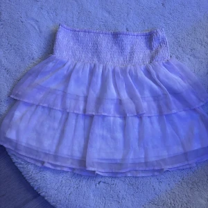 Vit/lila volangkjol med resårmidja - kort kjol i vitt/lila med två lager volanger och bred smockresår i midjan. 