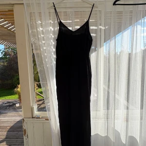 Svart långklänning från Divided - Svart långklänning från Divided med tunna axelband och v-ringad hals. Klänningen är i ett lätt, transparent tyg som ger en luftig känsla. Perfekt för dig som gillar minimalistisk och stilren look.